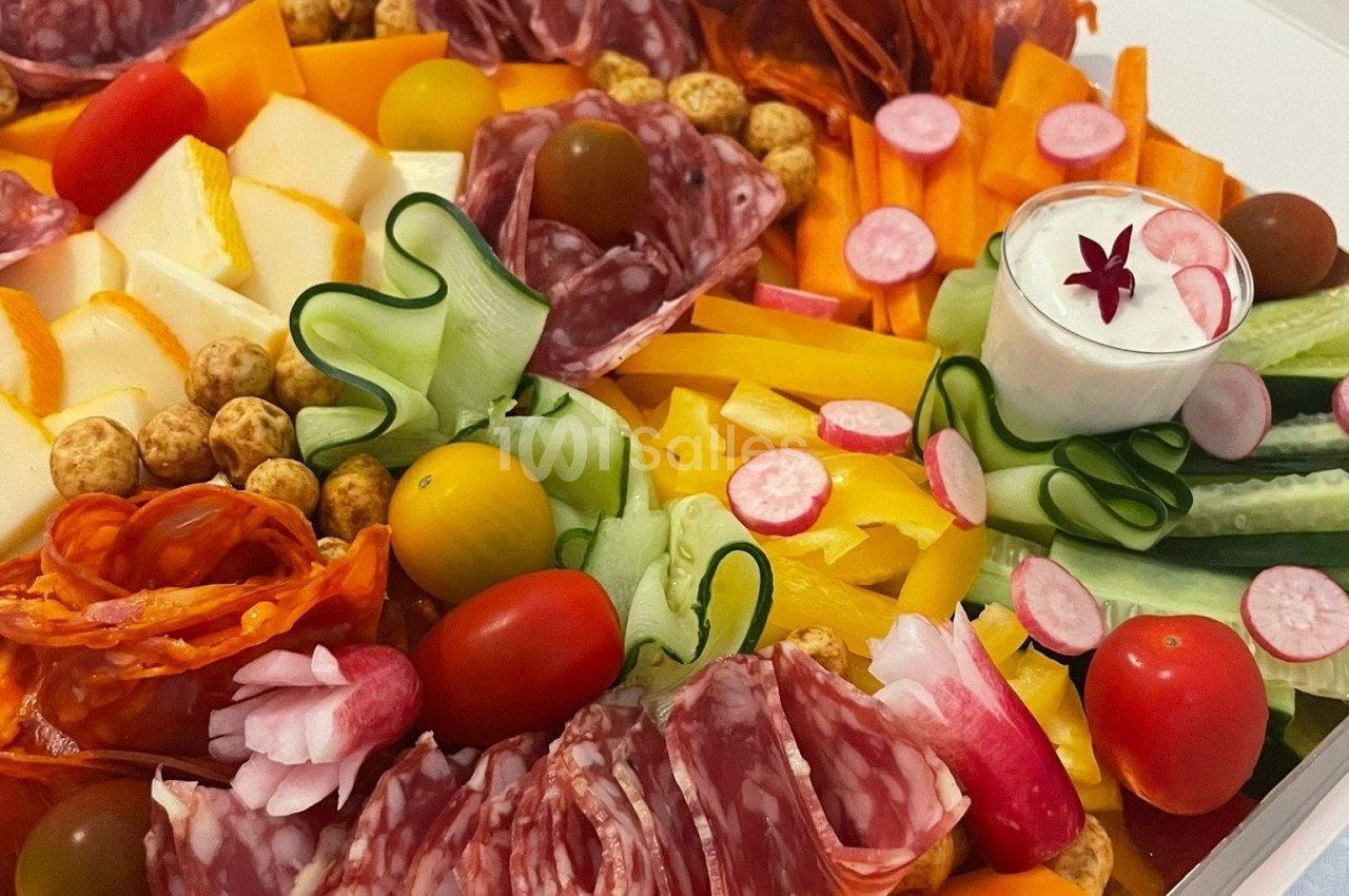 Plateau coloré composé de charcuteries, légumes frais, fromages, tomates cerises et une sauce blanche en accompagnement.