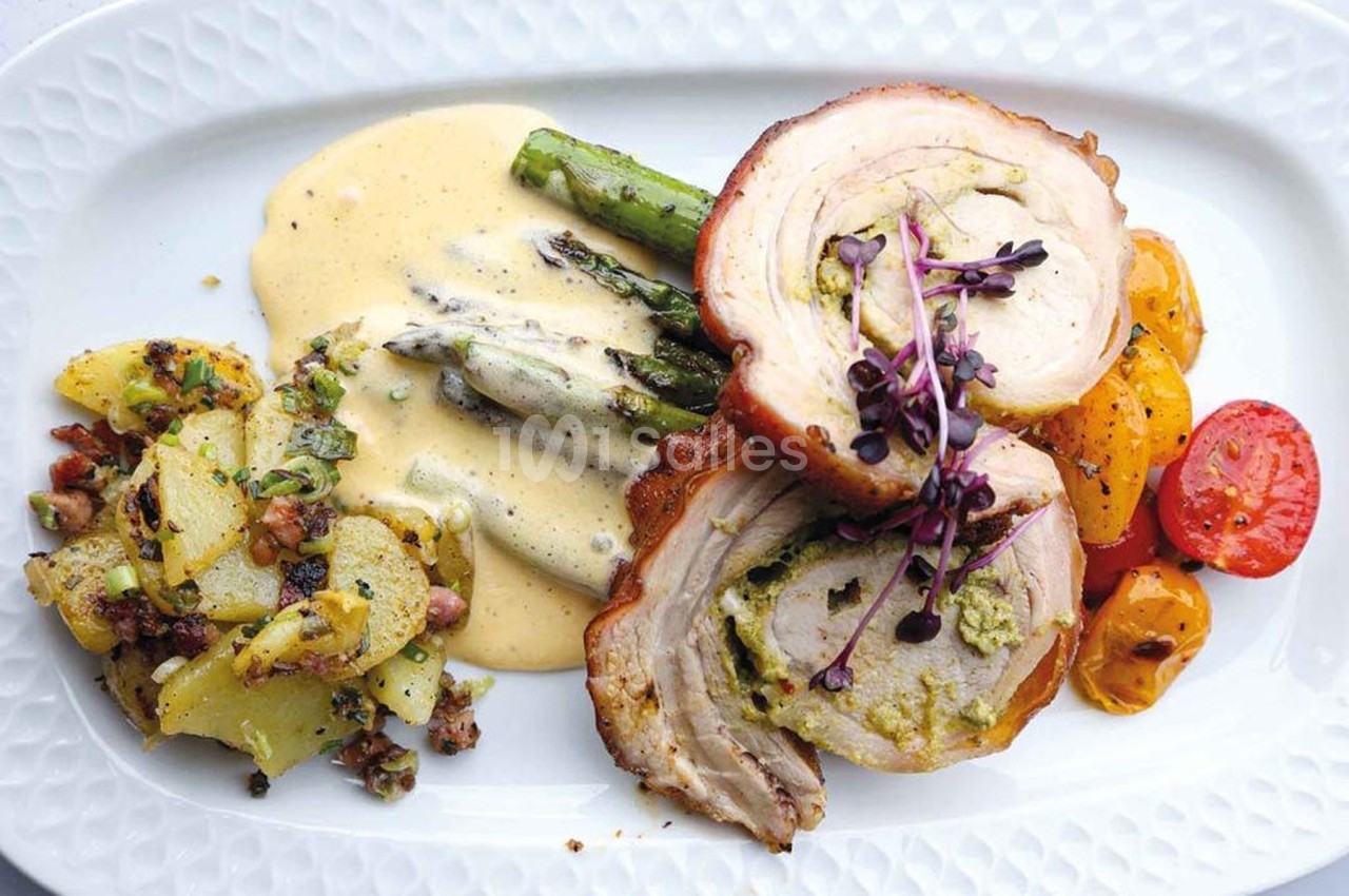 Assiette composée de rôti farci, asperges nappées de sauce, pommes de terre sautées et légumes rôtis.