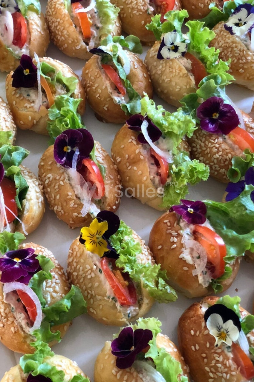 Petits pains garnis de salade, tomates, poisson et décorés de fleurs comestibles sur un plateau.