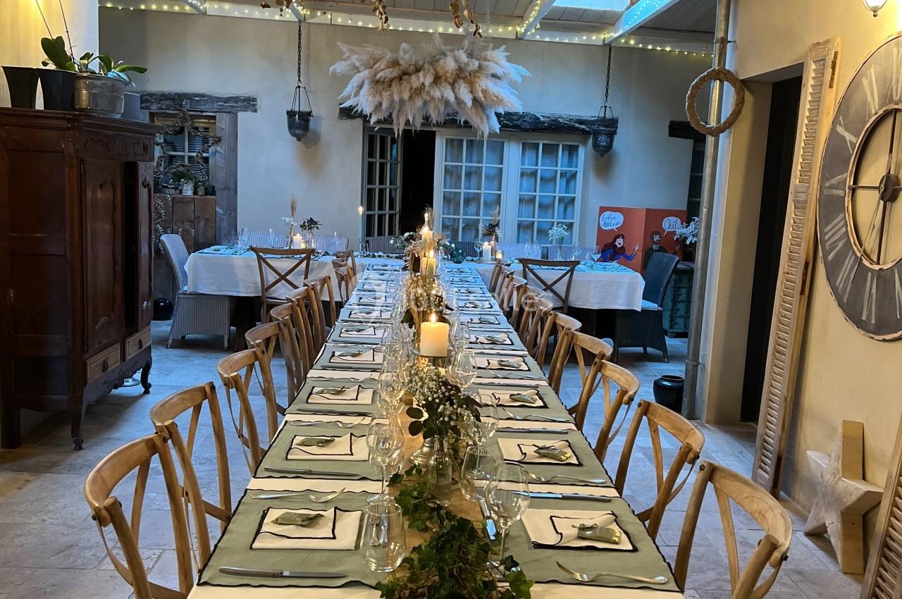 Grande table de banquet décorée de feuillage, bougies et vaisselle, dans une salle au plafond en bois éclairé.