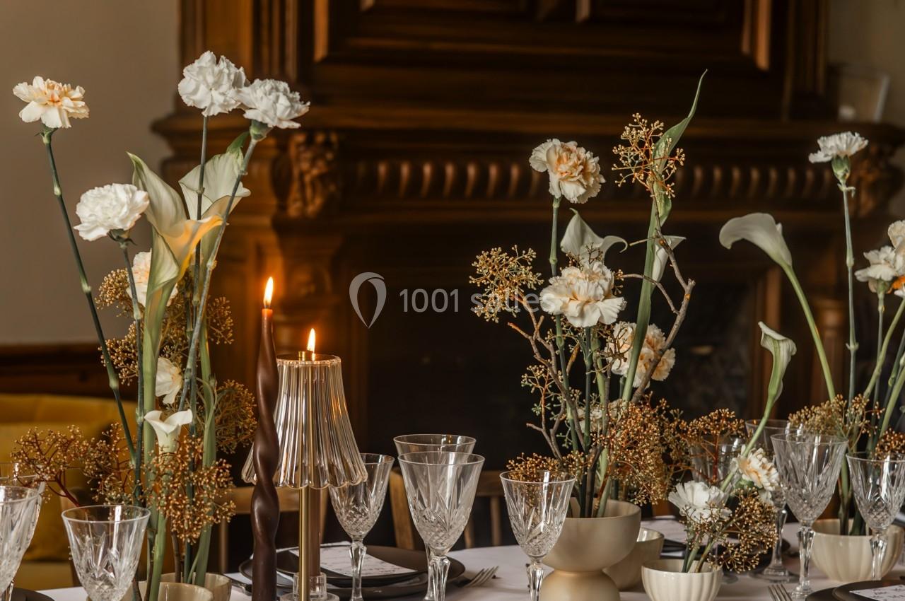 Table élégamment dressée avec nappe blanche, vaisselle raffinée, bougies allumées et compositions florales.