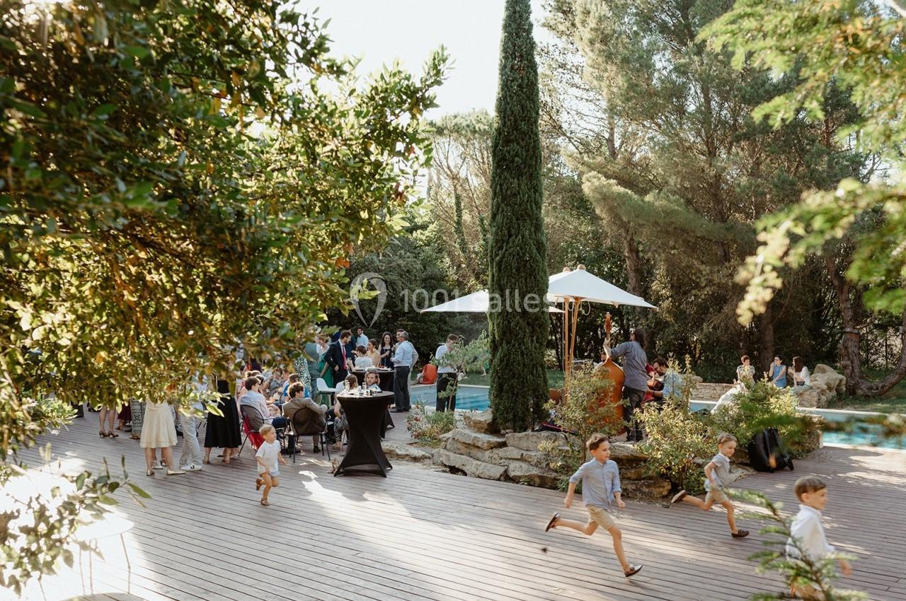Des enfants courent sur une terrasse en bois lors d'un événement en plein air, entouré de végétation et de convives.