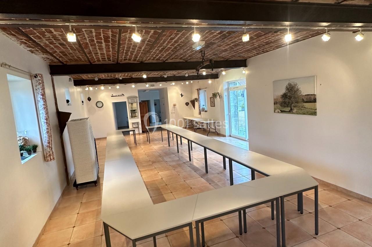 Salle lumineuse avec plafond en briques, tables disposées en U, carrelage au sol et grandes fenêtres donnant sur l'extérieur.