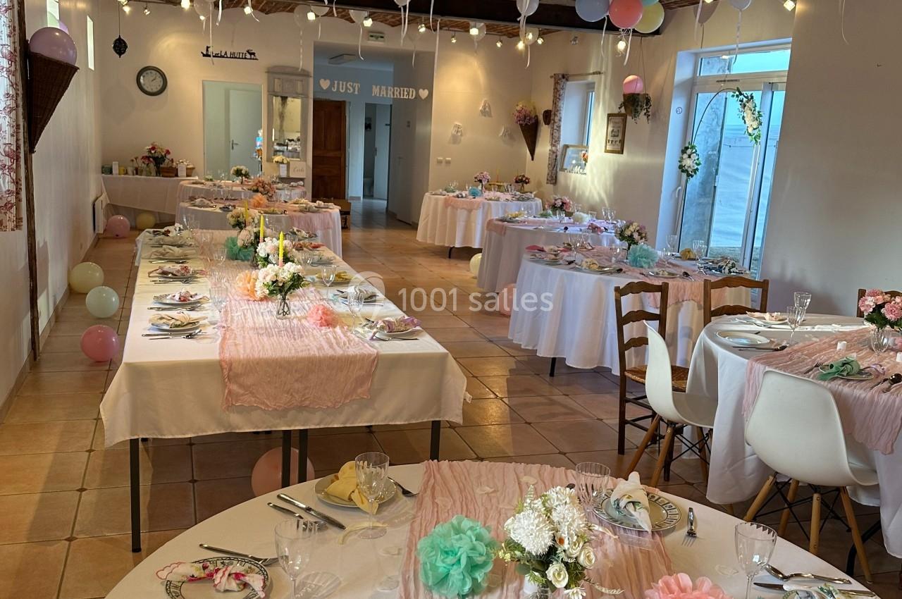 Salle décorée pour une réception avec tables dressées, nappes roses, ballons suspendus et ambiance festive.