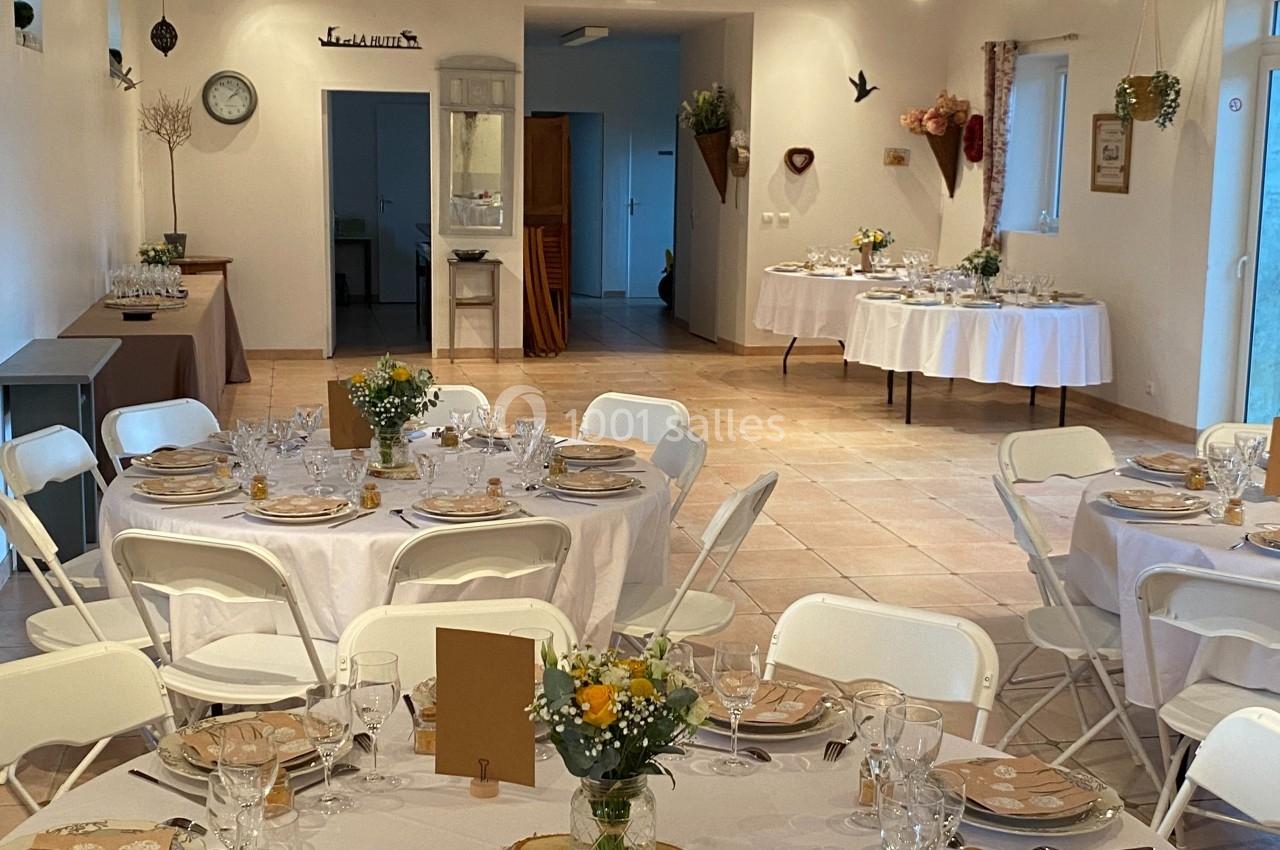 Salle de réception décorée avec des tables rondes dressées, nappes blanches, vaisselle élégante et fleurs en centre de table.