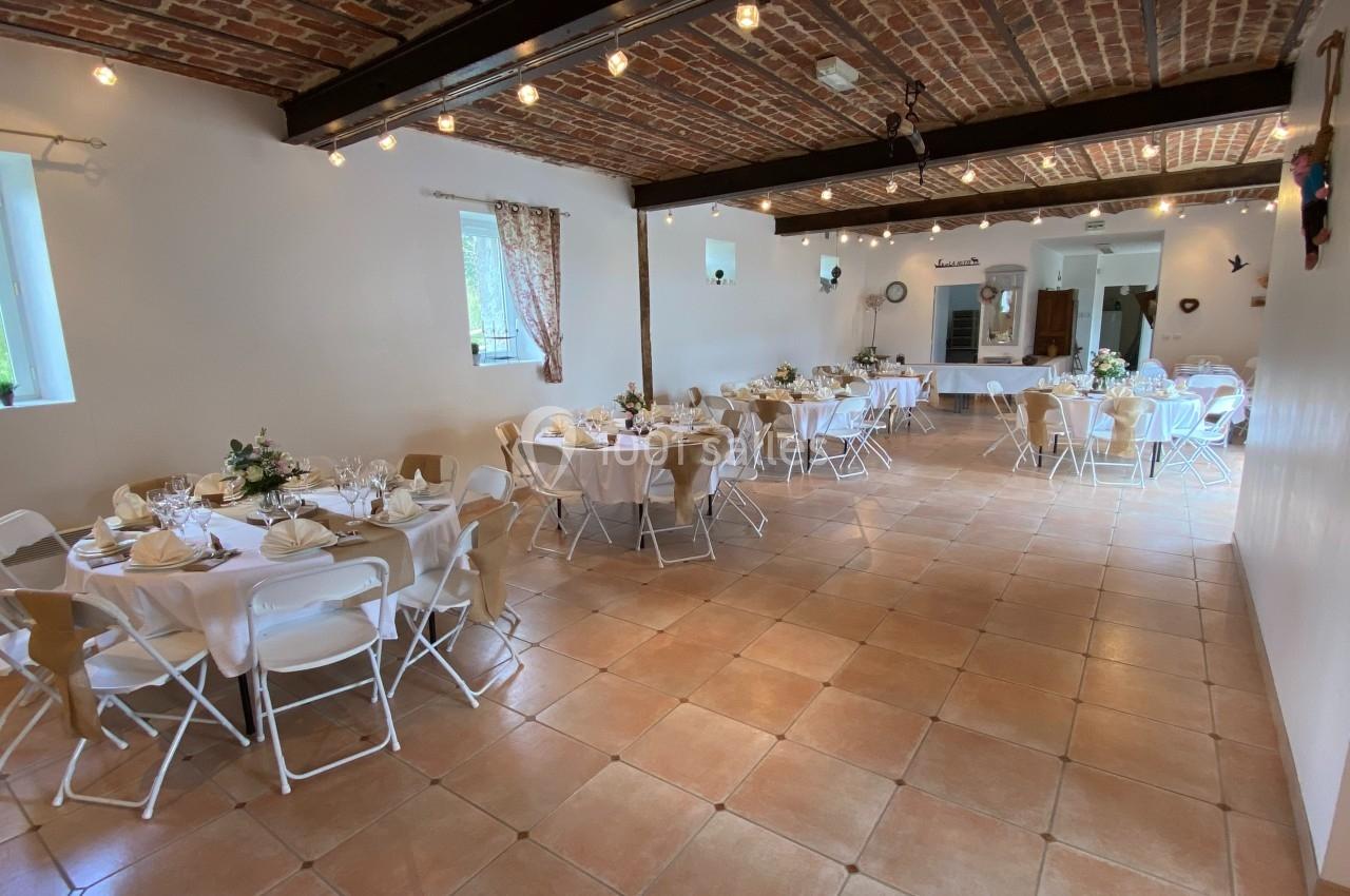 Salle de réception décorée avec des tables rondes dressées, chaises blanches et plafond en briques apparentes.