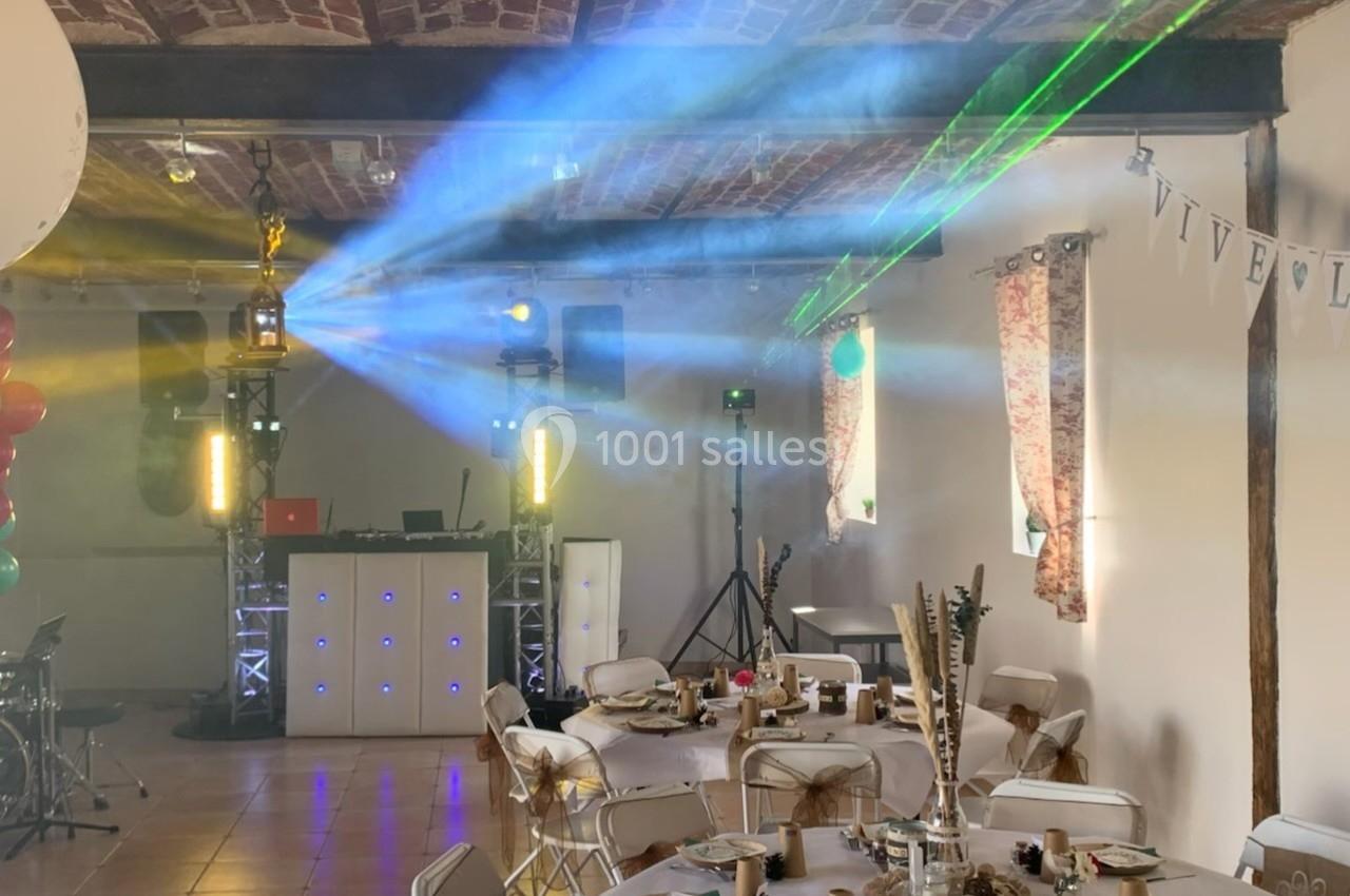 Salle décorée pour un événement, avec tables dressées, éclairages colorés et jeux de lumière projetés.