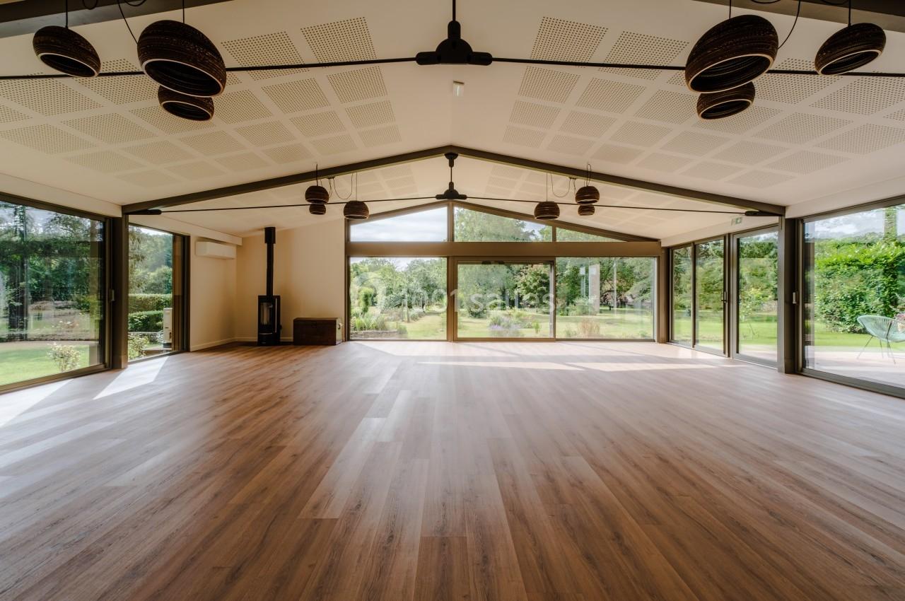 Salle lumineuse avec parquet en bois, grandes baies vitrées donnant sur un jardin verdoyant.