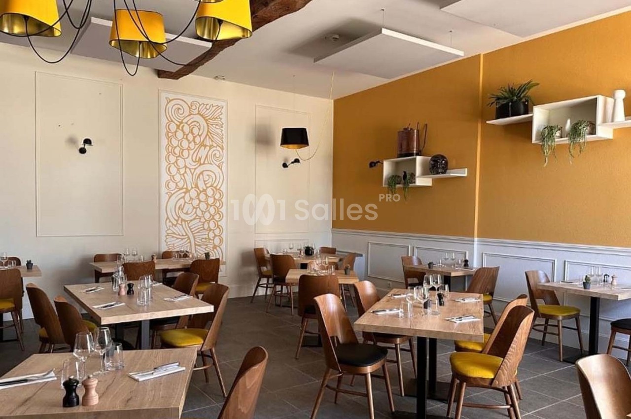 Salle de restaurant lumineuse avec tables en bois, chaises jaunes, décoration murale et étagères avec plantes.
