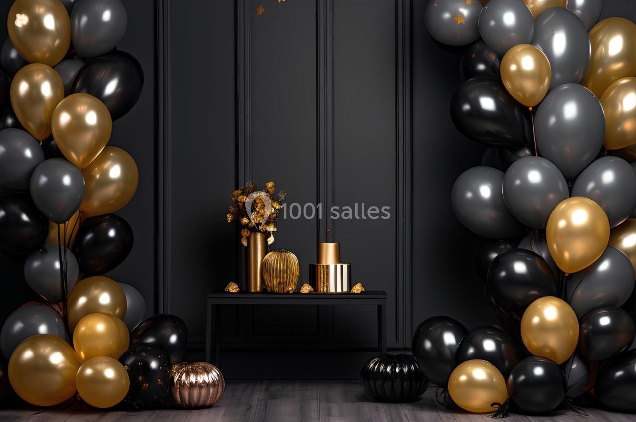 Décoration festive avec ballons noirs, dorés et gris, table ornée de fleurs et objets dorés sur fond mural sombre.