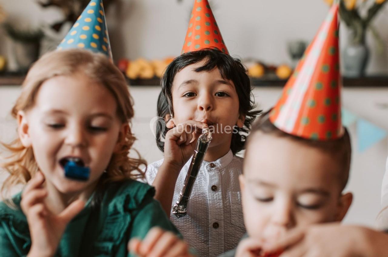 Des enfants portant des chapeaux de fête s'amusent en soufflant dans des cotillons dans une ambiance festive.