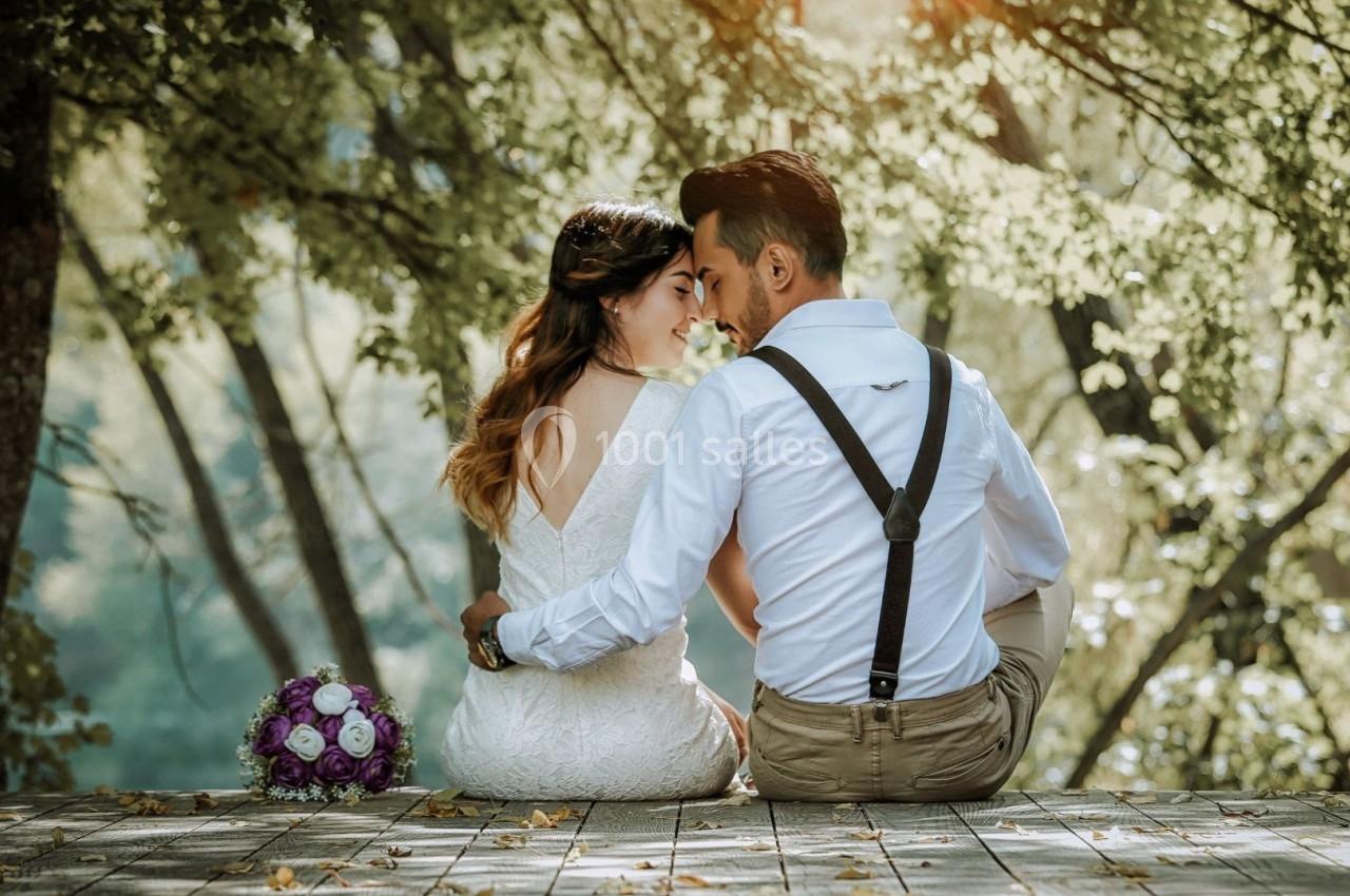 Un couple assis sur une terrasse en bois, entouré de verdure, avec un bouquet de fleurs posé à côté.
