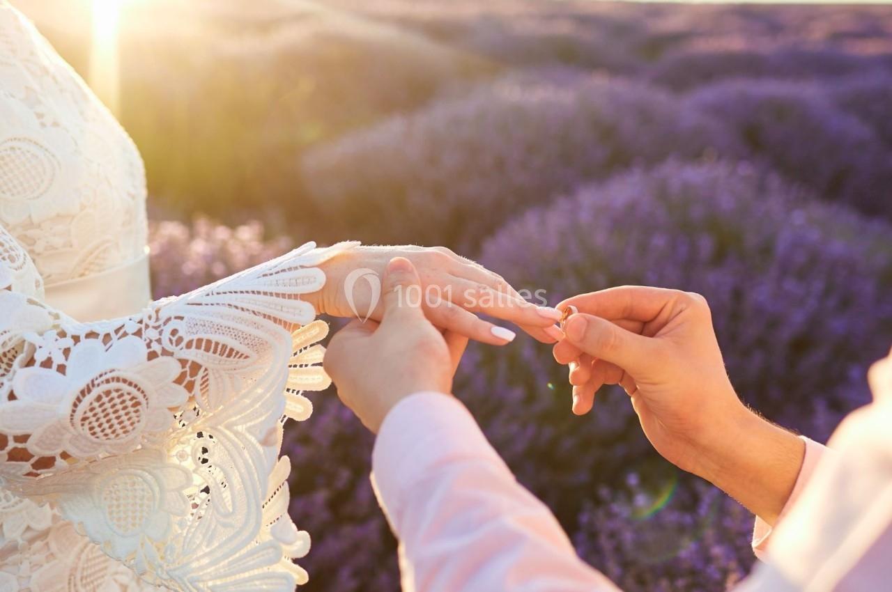 Une personne glisse une bague au doigt d'une autre dans un champ de lavande au coucher du soleil.