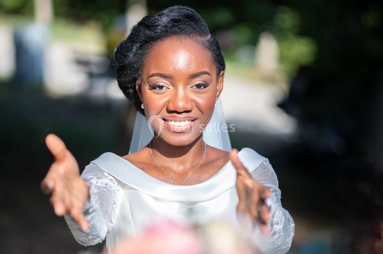Une femme en robe blanche tend les bras en avant, souriante, dans un environnement extérieur lumineux.