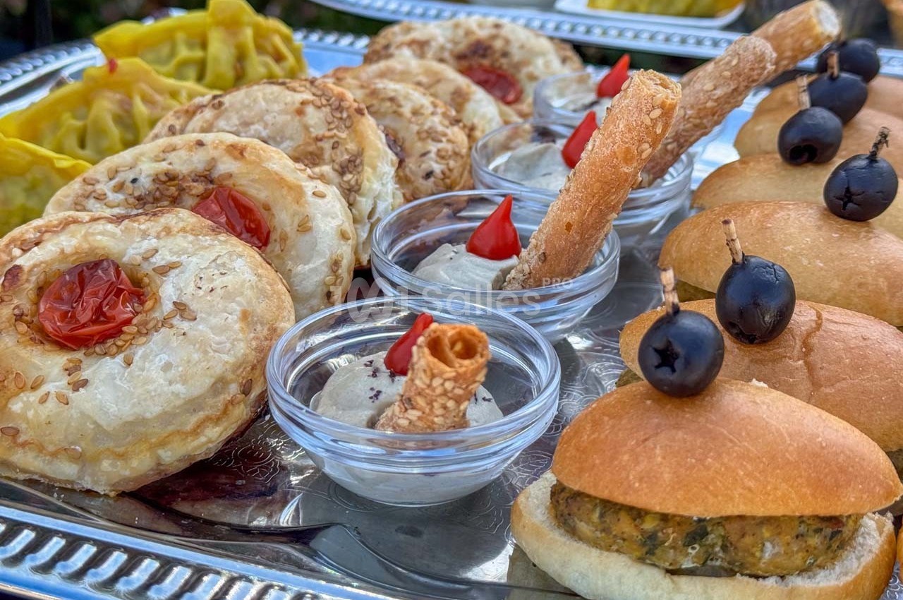 Plateau de bouchées salées variées comprenant feuilletés, mini-burgers, dips et olives noires.