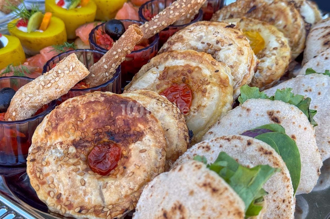 Plateau de bouchées variées comprenant feuilletés, wraps garnis, roulés de saumon et verrines colorées.
