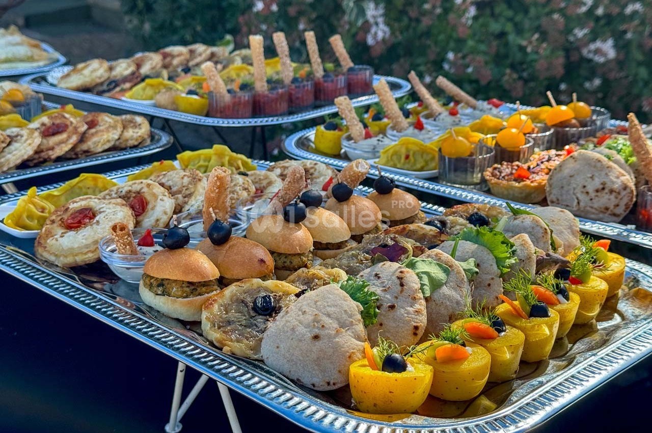 Plateaux garnis de mini-sandwichs, wraps, verrines et amuse-bouches variés présentés en extérieur.