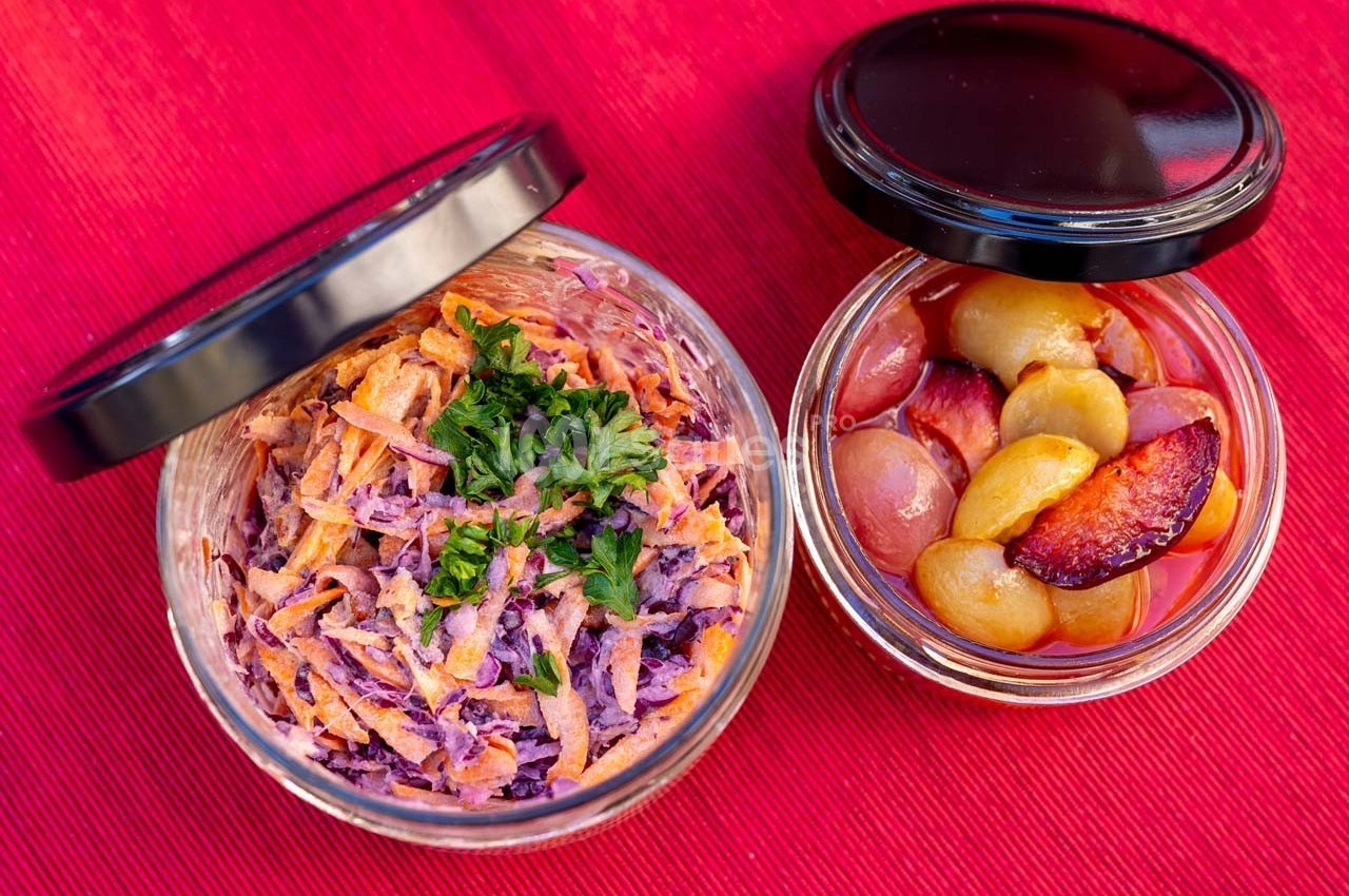 Deux bocaux ouverts contenant une salade de carottes et chou rouge garnie de persil, et des fruits marinés.