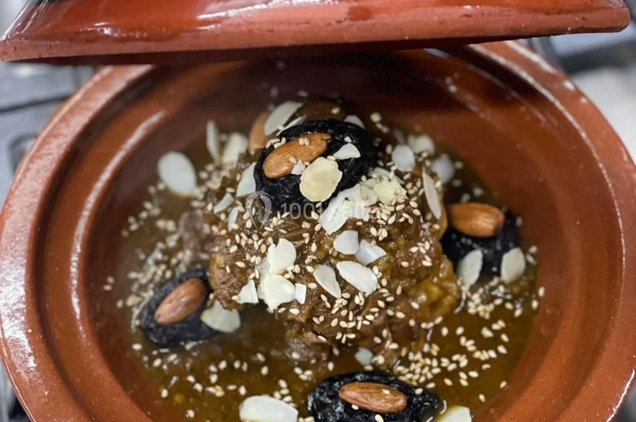 Tajine marocain avec viande, pruneaux, amandes, graines de sésame et amandes effilées, présenté dans un plat en terre cuite.