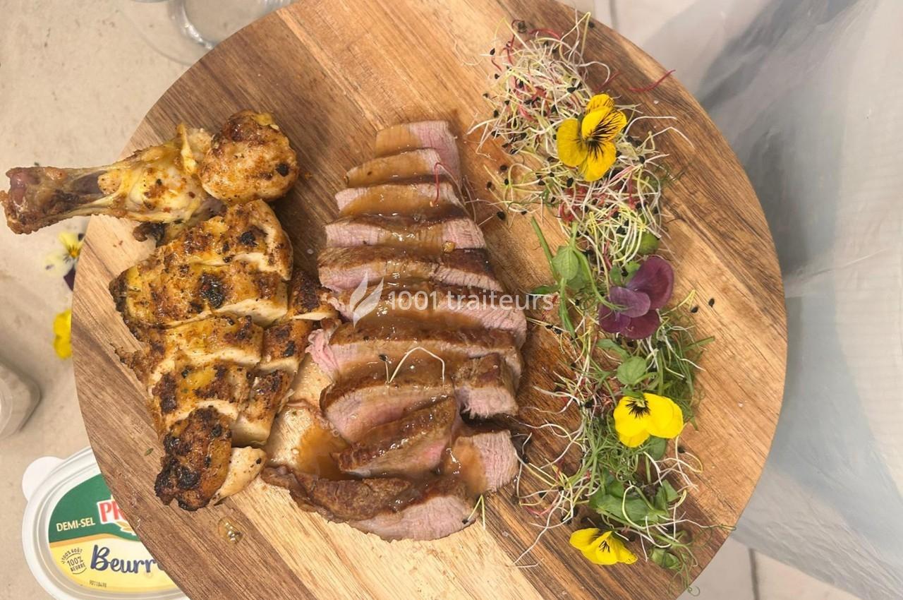 Assiette en bois avec cuisse de poulet grillée, tranches de viande sauce, jeunes pousses et fleurs comestibles.