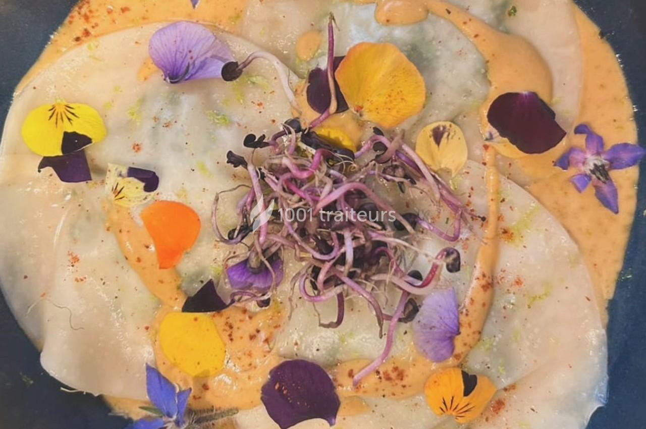 Assiette de ravioles garnies, décorées de fleurs comestibles colorées et de pousses, servies avec une sauce crémeuse.