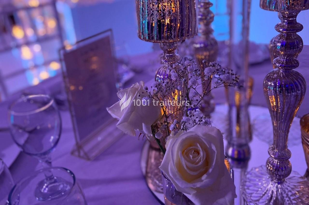 Centre de table avec roses blanches, gypsophiles et chandeliers dorés éclairés dans une ambiance tamisée.