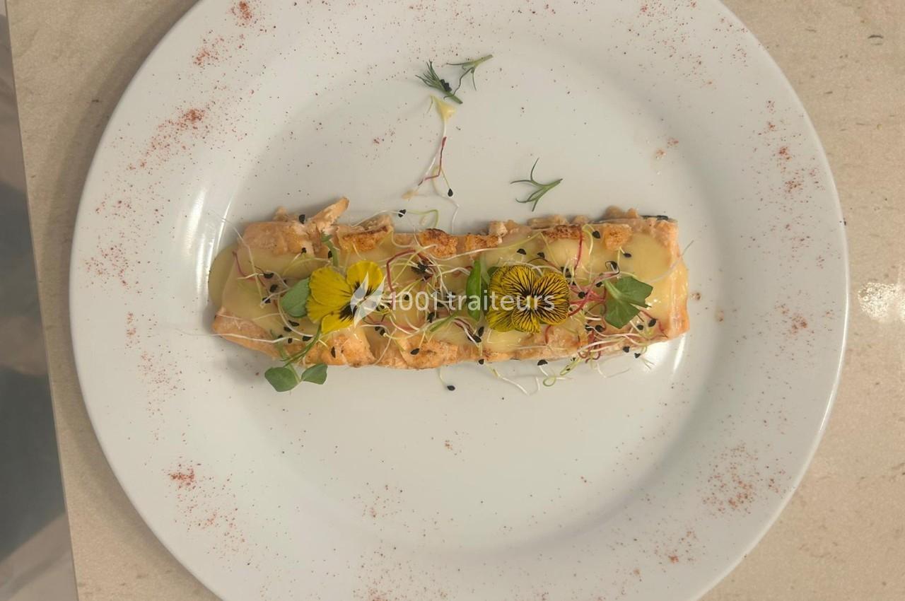 Assiette contenant un plat de saumon grillé garni de sauce, fleurs comestibles et pousses, sur lit de poudre épicée.