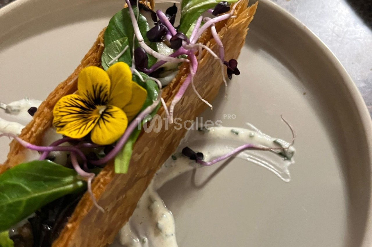 Feuilleté garni de légumes verts, pousses et fleur comestible, servi sur une sauce blanche parsemée d'herbes.