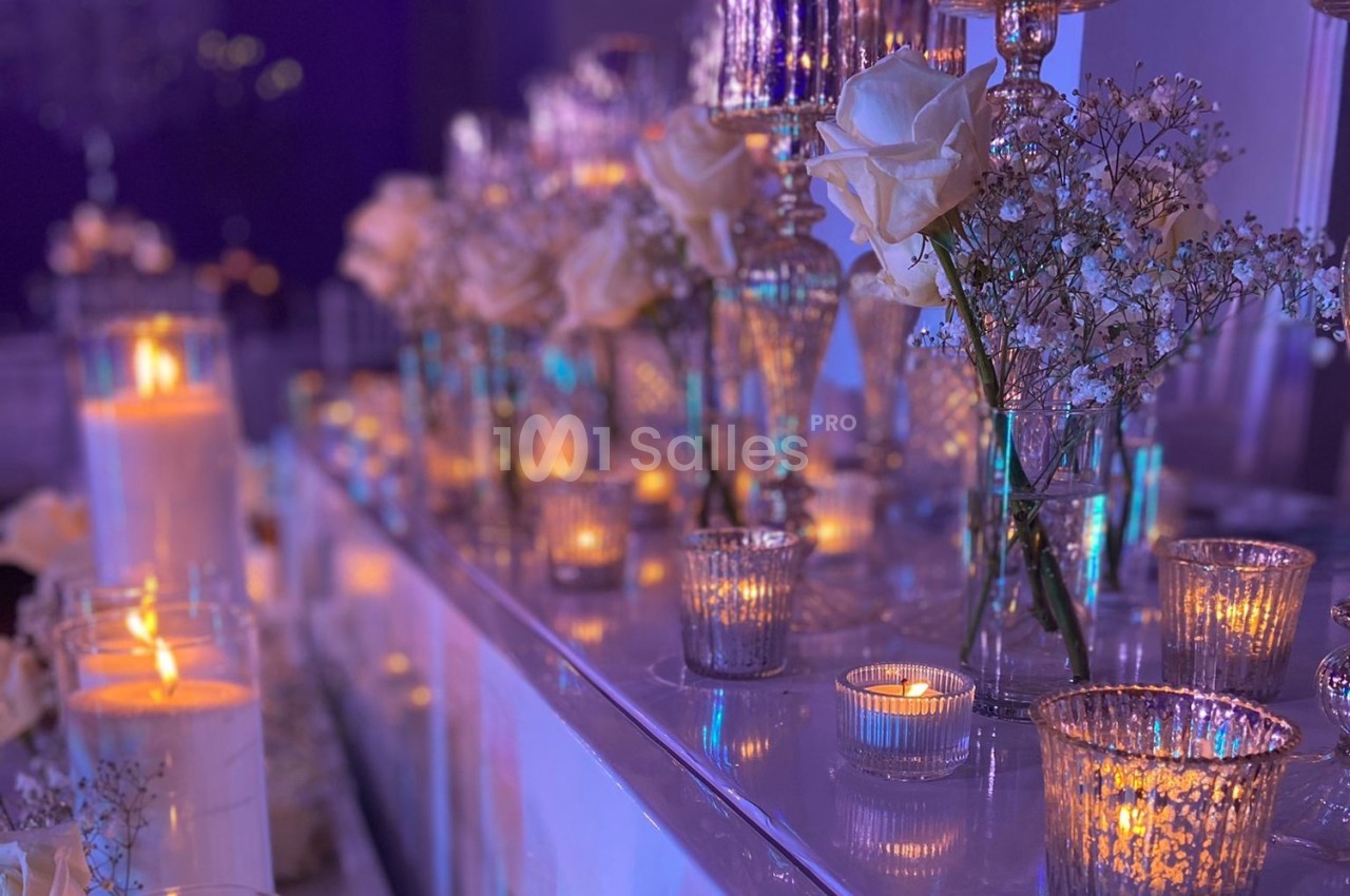 Bougies allumées et fleurs blanches disposées sur une table décorée pour un événement dans une ambiance tamisée.