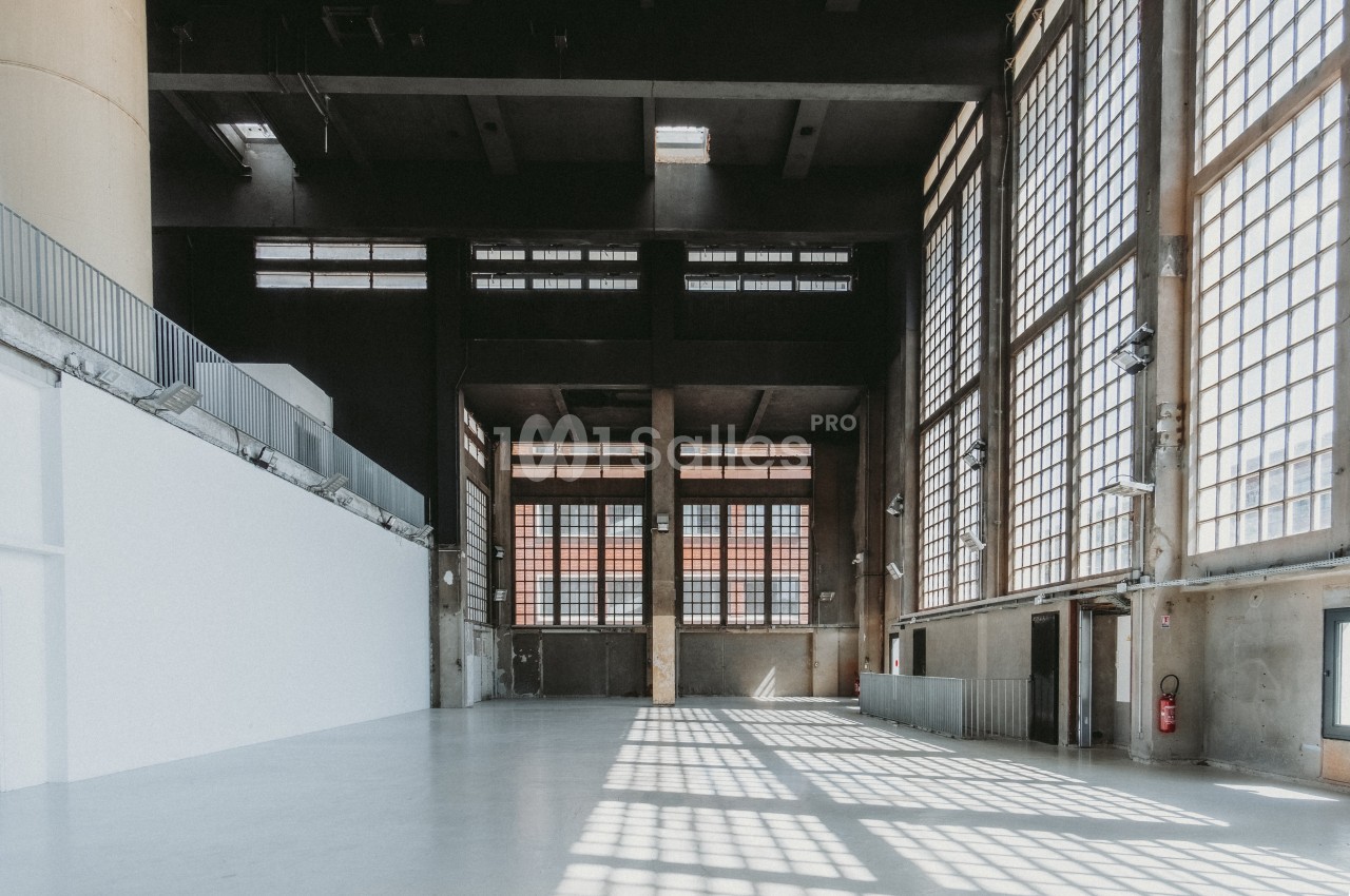 Intérieur d'un grand bâtiment industriel avec de hautes fenêtres laissant entrer la lumière naturelle.