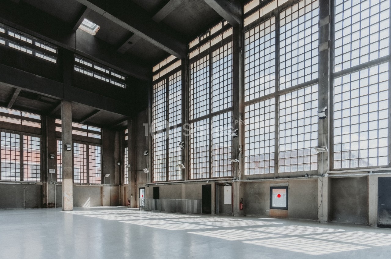 Intérieur d'un grand bâtiment industriel avec de hautes fenêtres en grille laissant entrer la lumière naturelle.