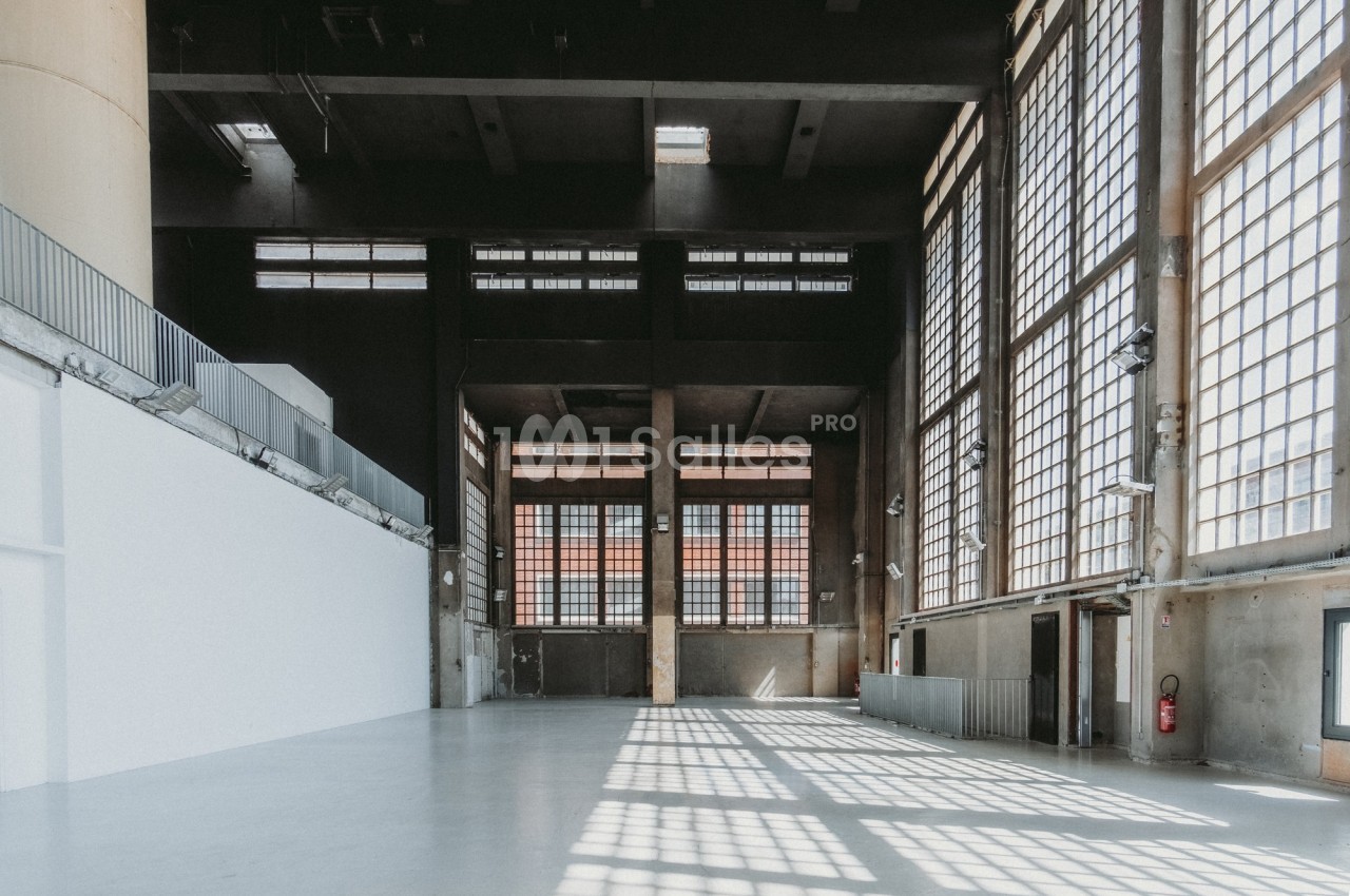 Intérieur d'un grand bâtiment industriel avec de hautes fenêtres laissant entrer la lumière naturelle.