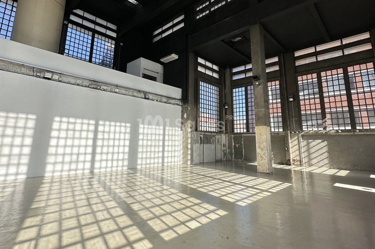 Intérieur d'un grand espace industriel avec des murs en béton, des colonnes et de grandes fenêtres laissant entrer la…