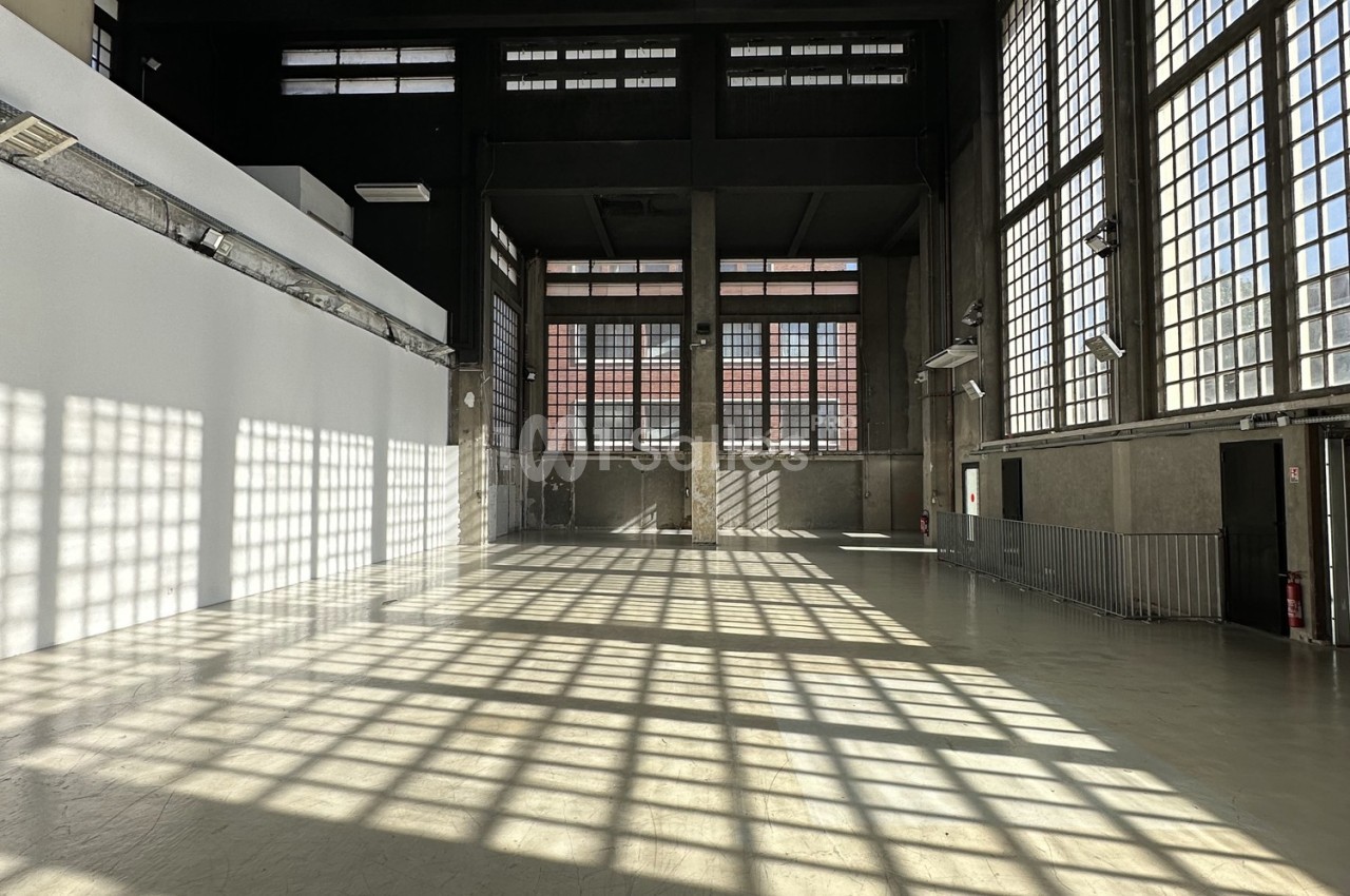 Intérieur d'un grand bâtiment industriel avec de larges fenêtres laissant entrer une lumière naturelle abondante.