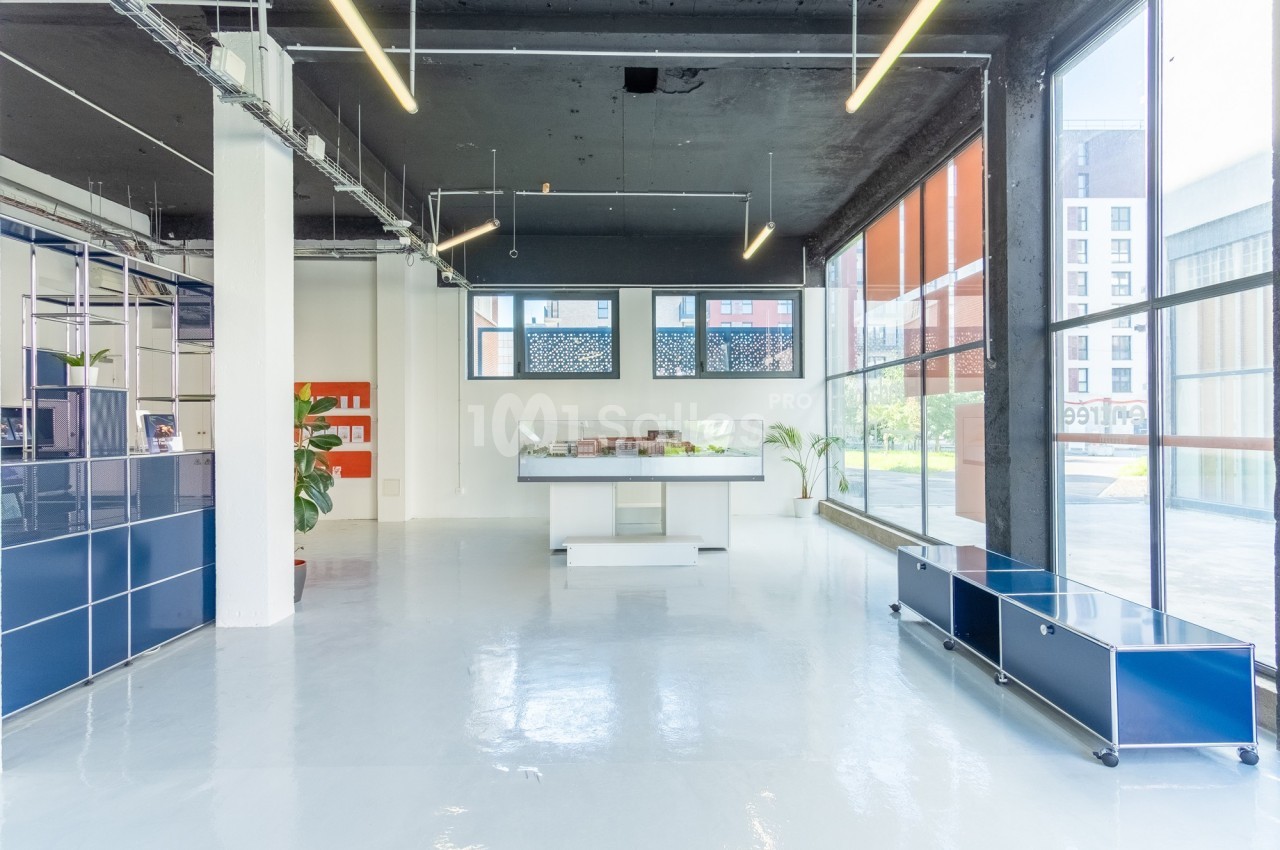 Intérieur lumineux d'un espace moderne avec sol blanc, mobilier minimaliste et grandes baies vitrées.