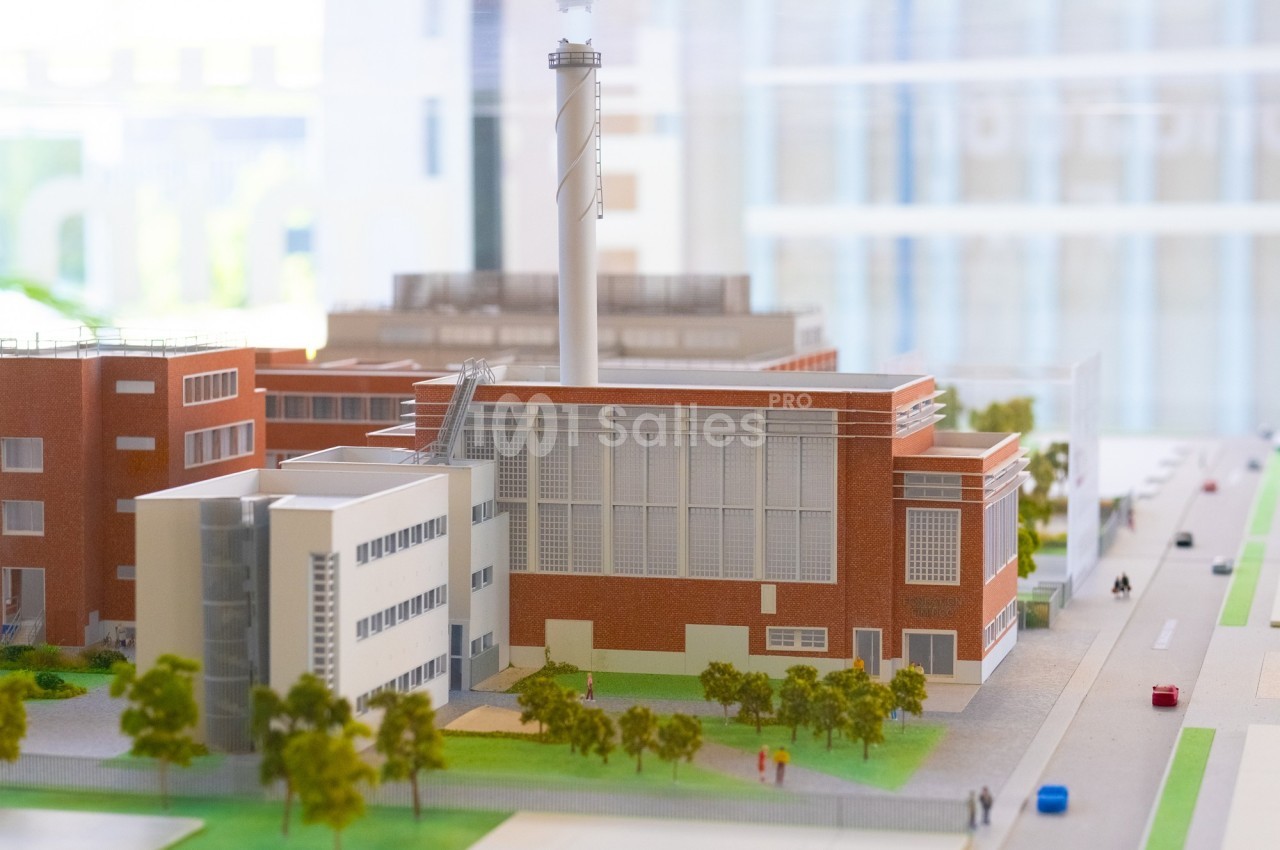 Maquette d'un complexe industriel en briques rouges avec une cheminée, entouré d'arbres et de rues.