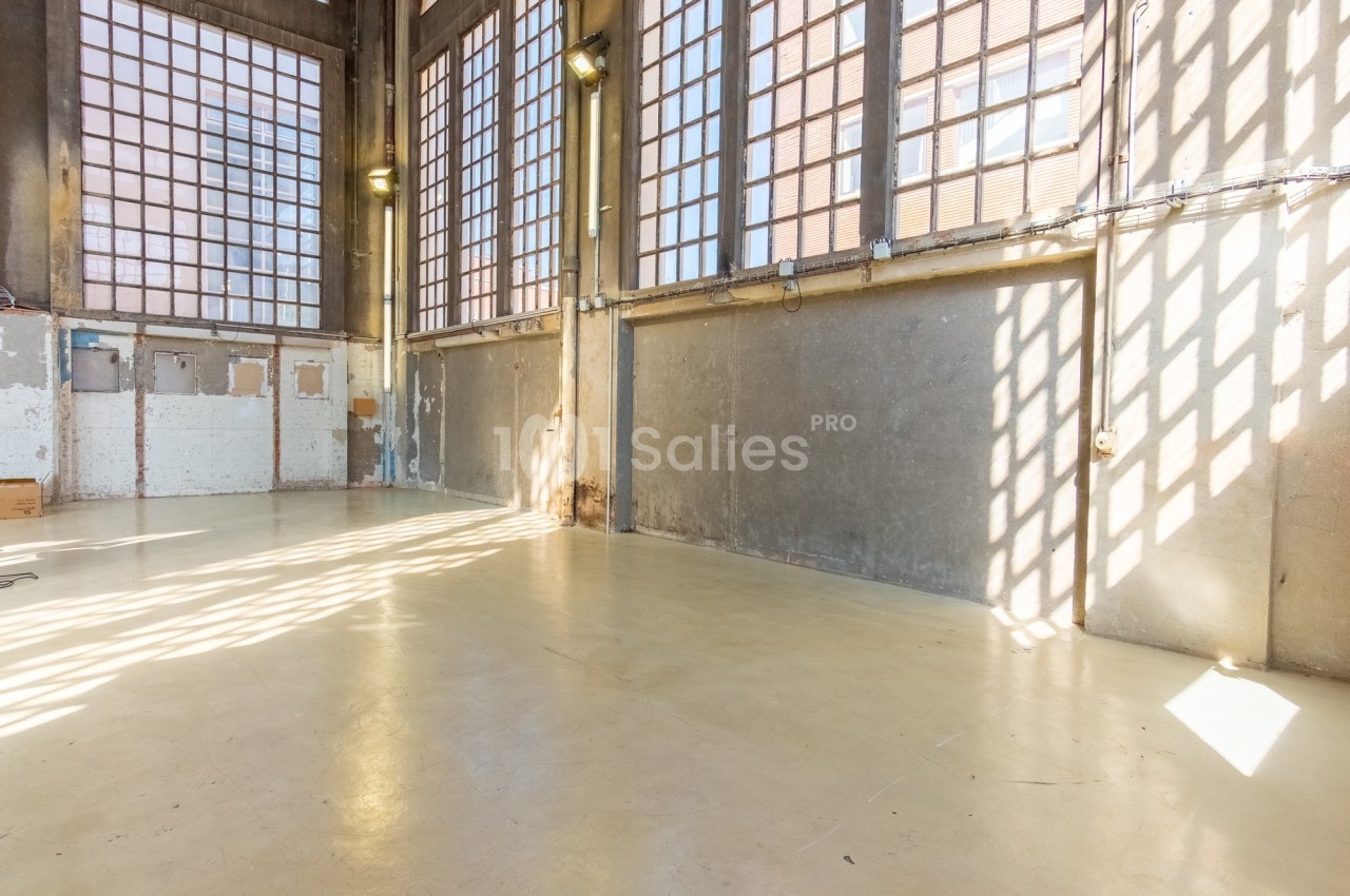Intérieur d'un grand espace industriel vide avec sol en béton, murs en béton brut et larges fenêtres laissant entrer la…