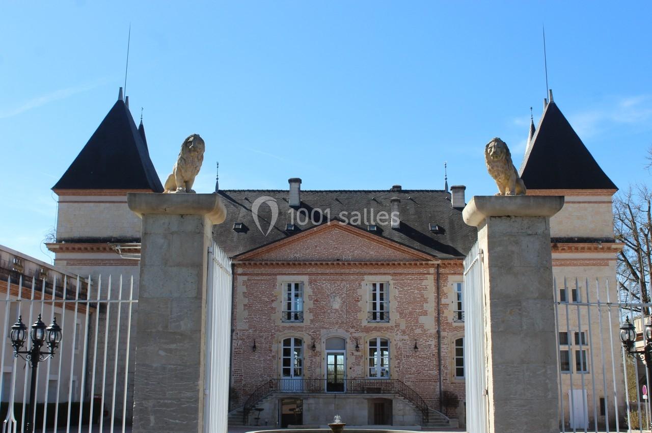 Façade d'un château en briques rouges avec deux tours, encadré par des piliers ornés de statues de lions.