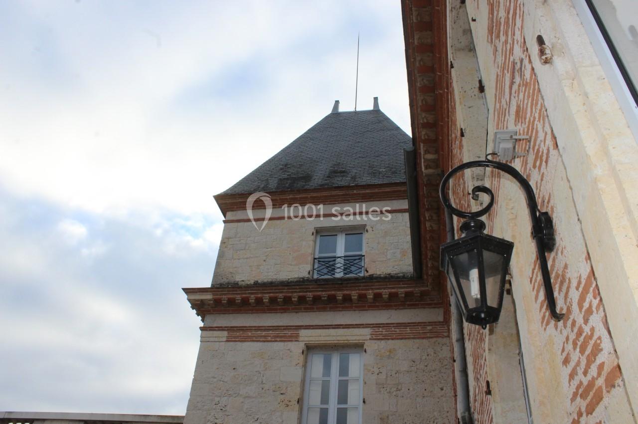 Façade en pierre d'un bâtiment ancien avec une tour, des briques apparentes et une lanterne murale noire.