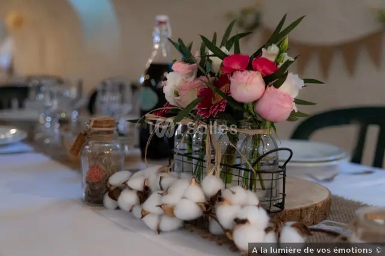 Centre de table avec bouquet de fleurs roses et blanches, branches de coton et décorations en verre sur une table dressée.