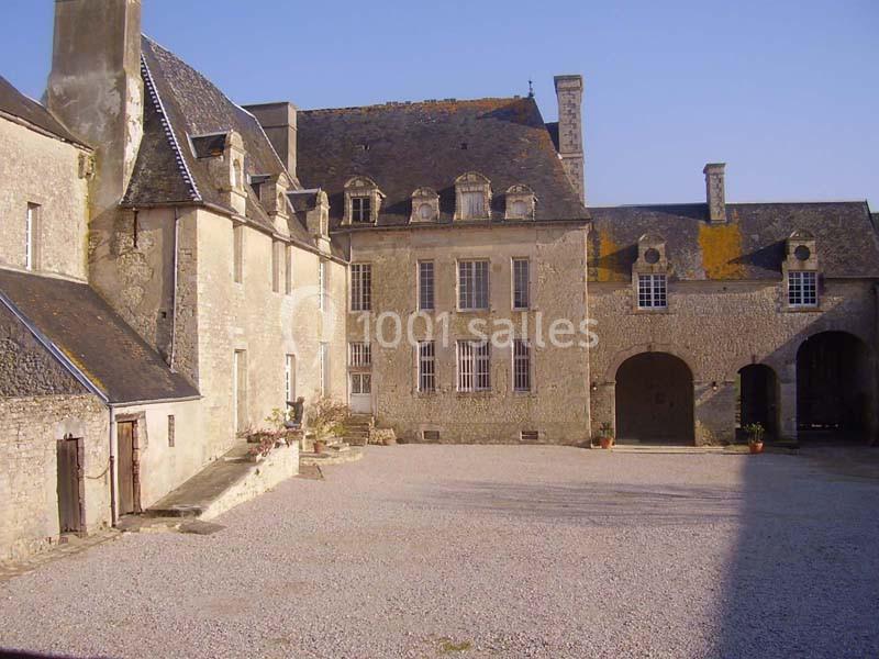 Cour intérieure d'un bâtiment historique en pierre avec toits en ardoise, fenêtres à petits carreaux et ciel dégagé.