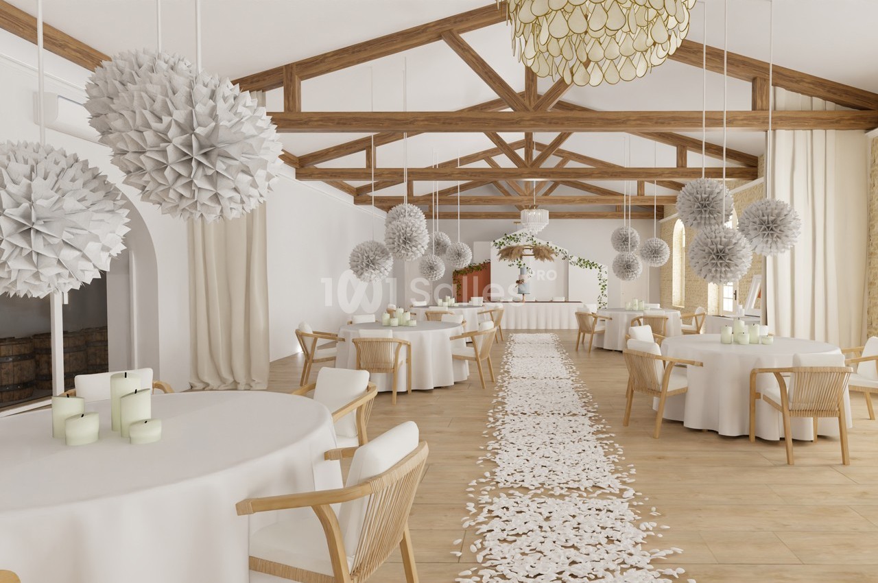 Salle de réception lumineuse avec tables rondes décorées, guirlandes suspendues et allée ornée de pétales blancs.
