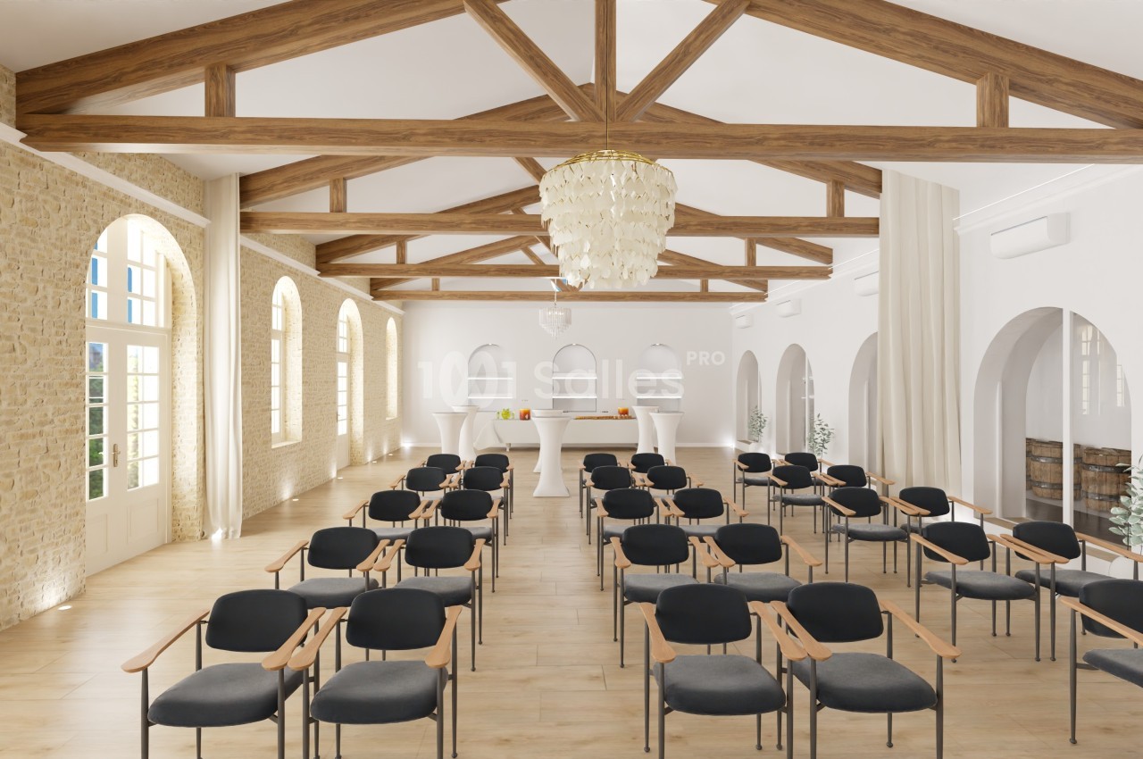 Salle lumineuse avec poutres apparentes, rangées de chaises noires et un bar en fond sous un lustre élégant.