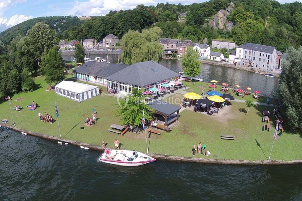 Vue aérienne d'un espace de détente au bord d'une rivière avec pelouse, terrasses, parasols et quelques visiteurs.