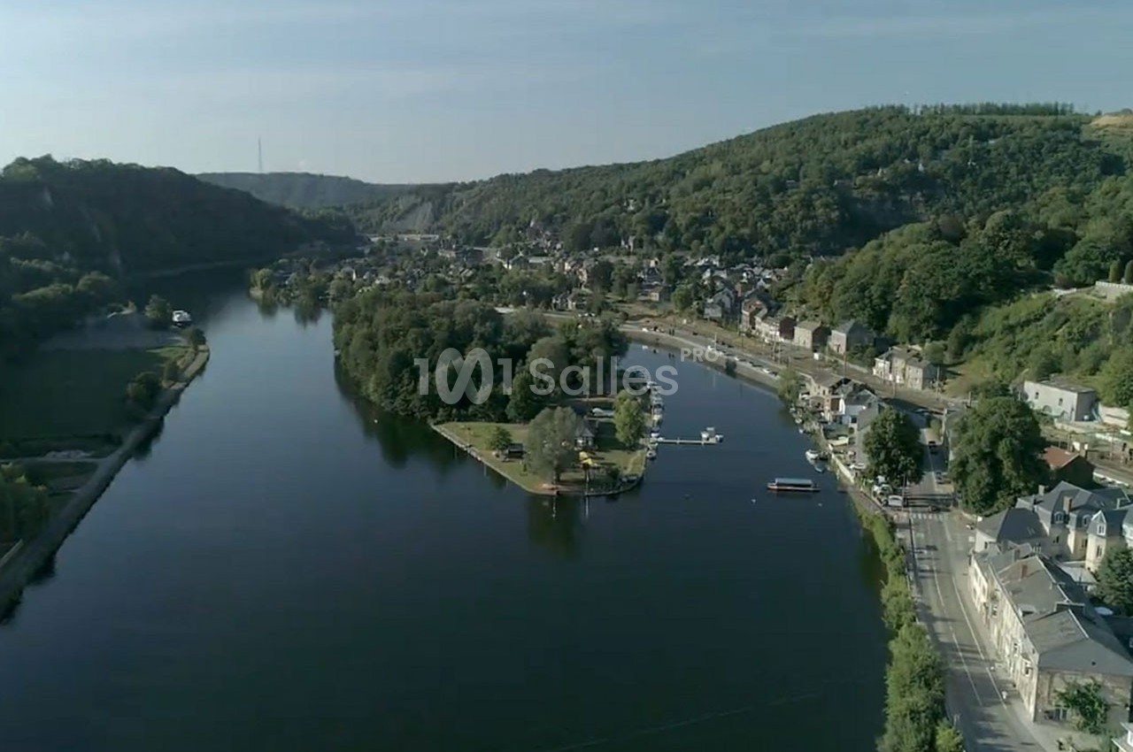Vue aérienne d'une rivière entourée de collines boisées, avec un village et un quai au bord de l'eau.