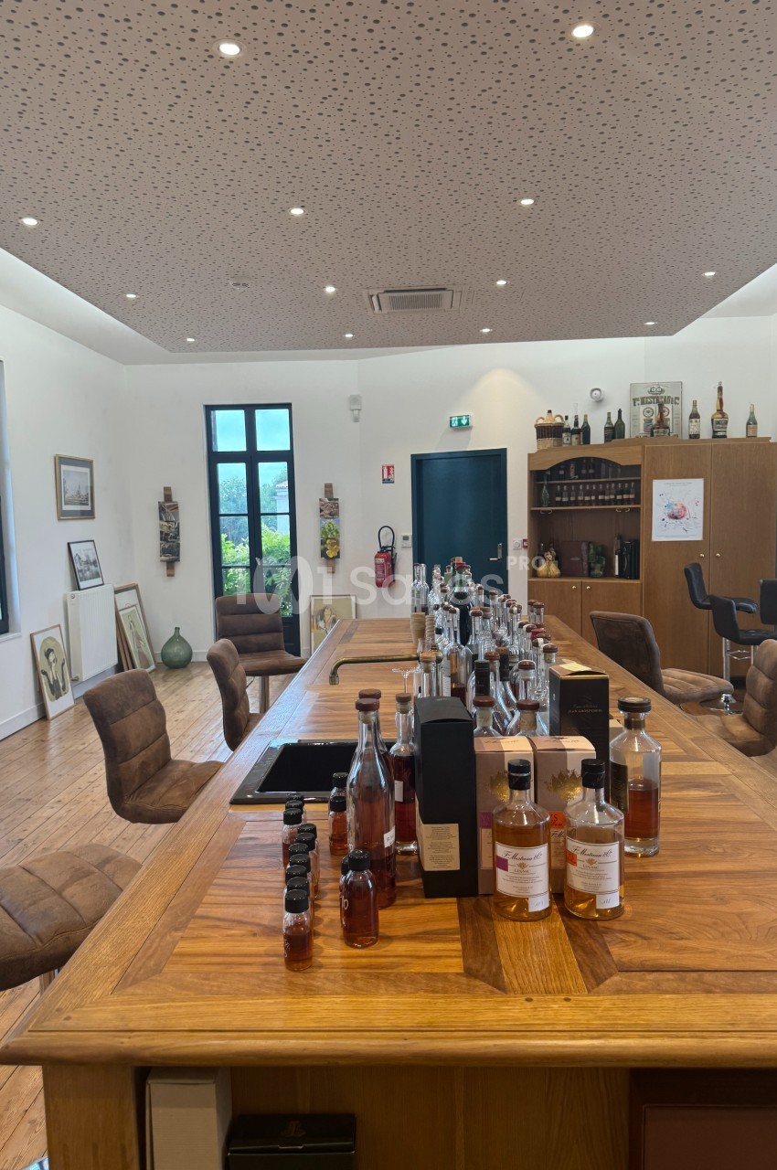 Salle de dégustation avec une grande table en bois garnie de bouteilles d'alcool, entourée de chaises.
