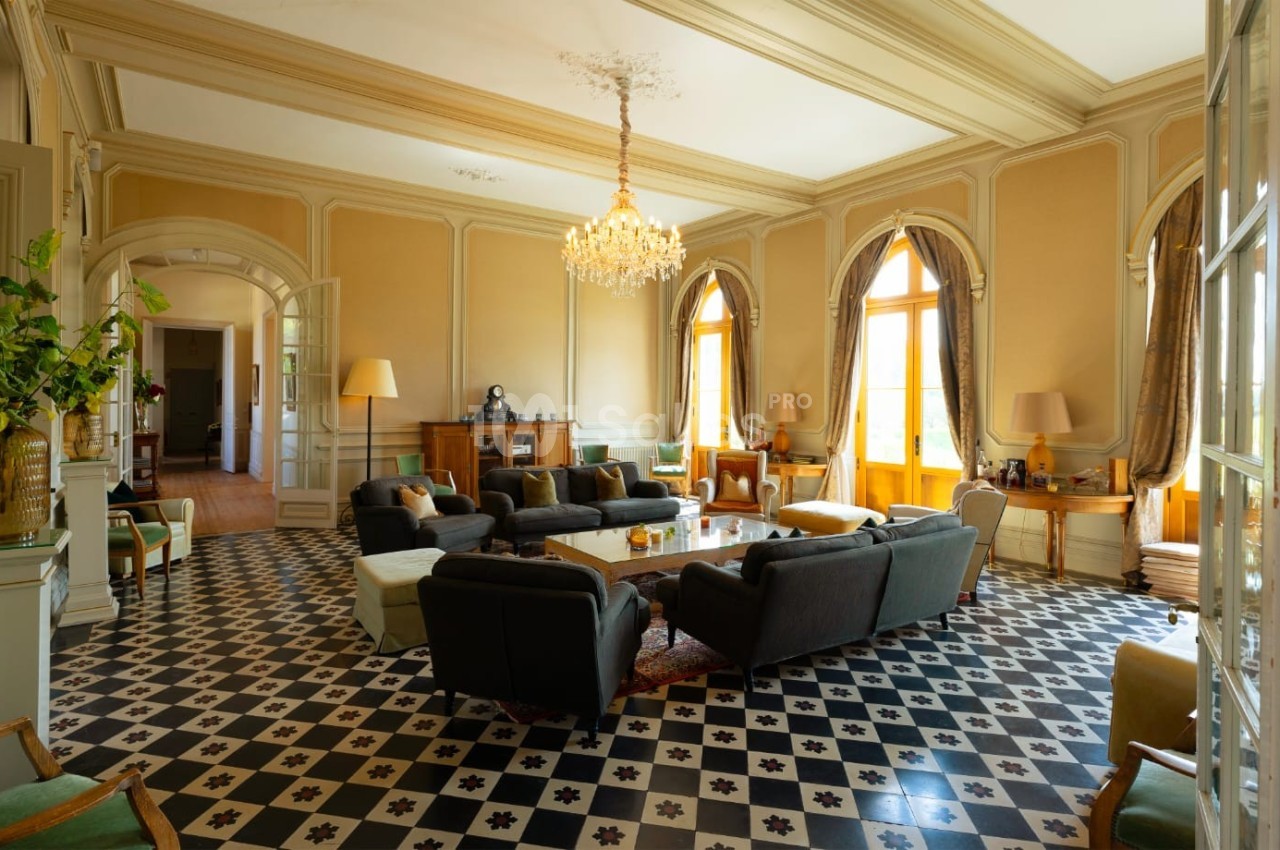 Salon spacieux avec parquet en damier noir et blanc, mobilier élégant et lustre central, baigné de lumière naturelle.