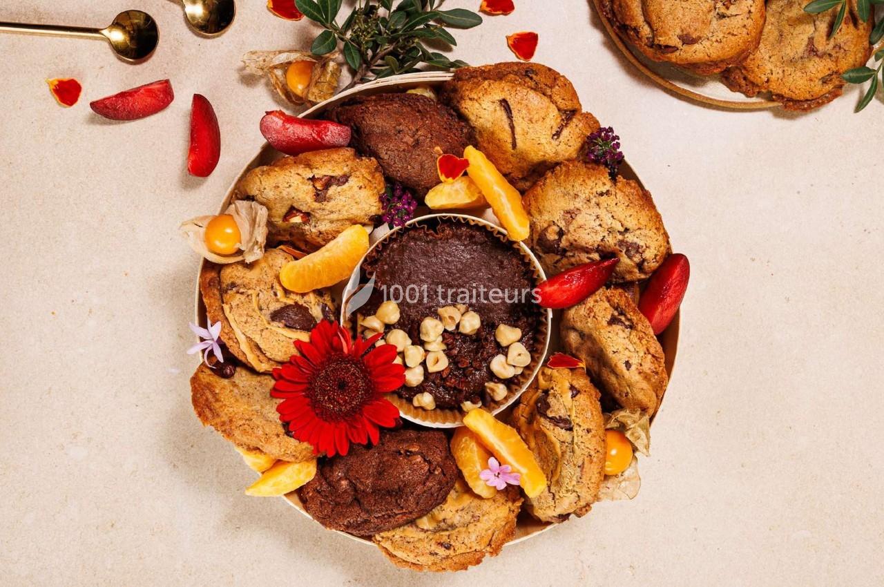 Assortiment de biscuits et muffins entouré de fruits, fleurs et décorations sur une table beige.