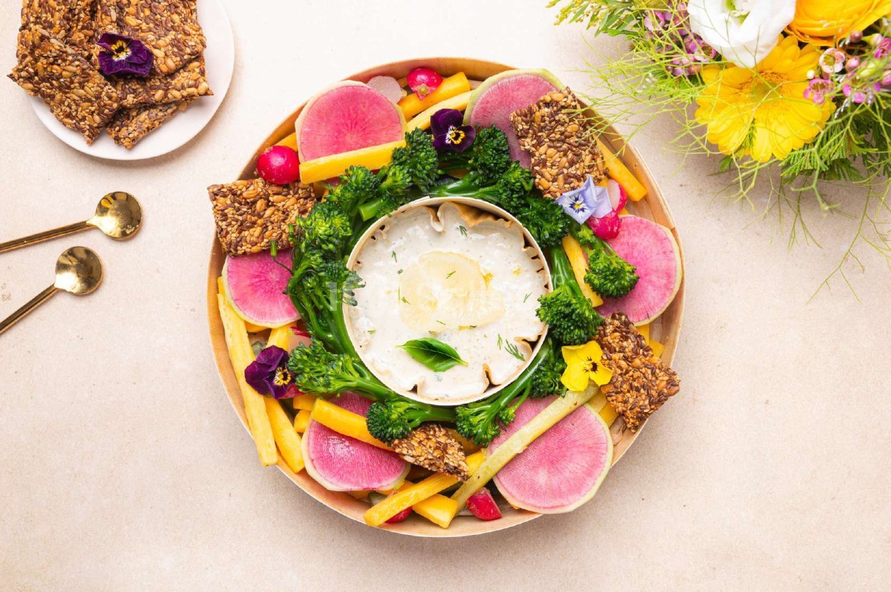 Plateau de légumes colorés avec dip au centre, entouré de crackers et décoré de fleurs comestibles.
