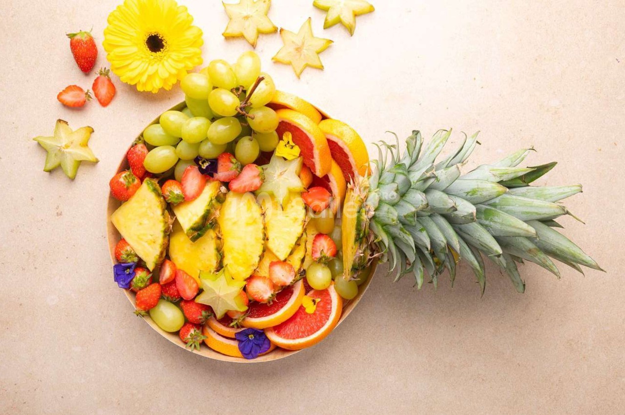 Assortiment de fruits frais comprenant ananas, fraises, raisins, oranges, caramboles et fleurs comestibles sur une table…